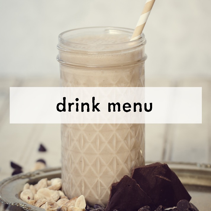 Frosted glass of creamy smoothie with a striped straw on a tray next to hazelnuts and chocolate chunks. Overlay text reads "drink menu." Cozy and inviting.
