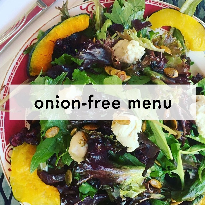 A colorful salad featuring mixed greens, pumpkin slices, seeds, and dollops of soft cheese. Text overlay reads "onion-free menu." Vibrant and fresh.