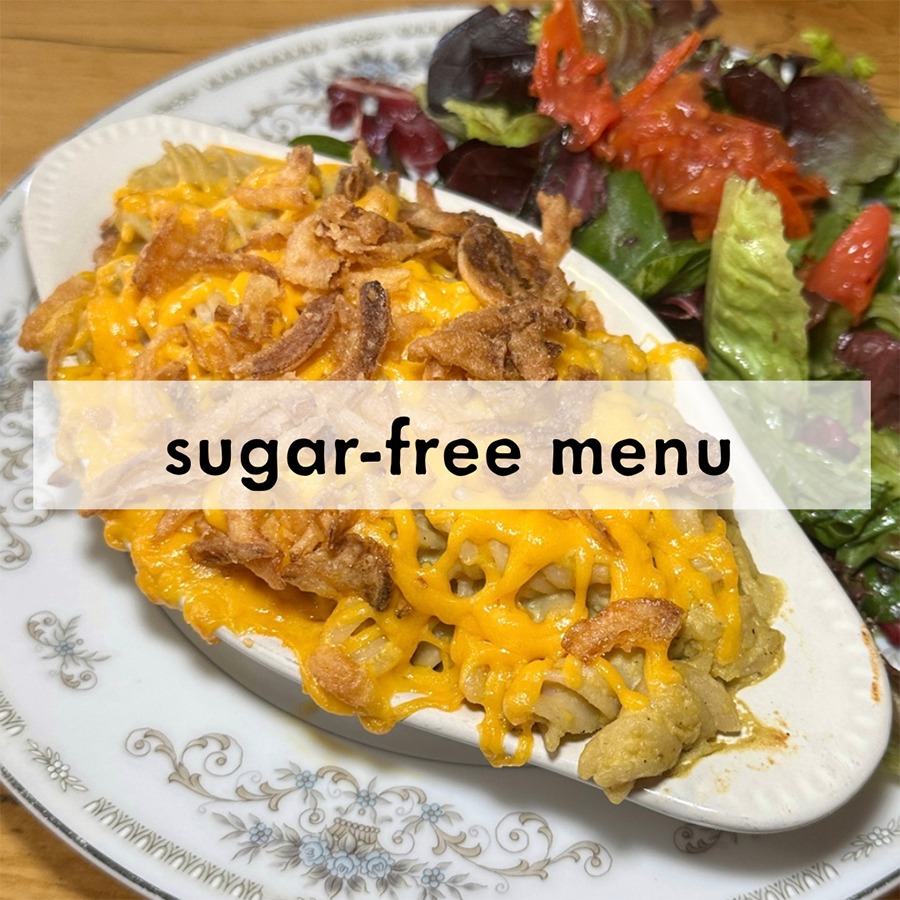 Oval dish of cheesy casserole with crispy onions on a vintage plate, paired with a fresh salad. Text overlay reads "sugar-free menu."